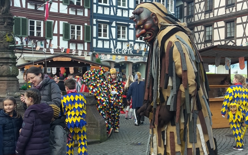 Narr mit Fratzenmaske vor Fachwerkhäuser